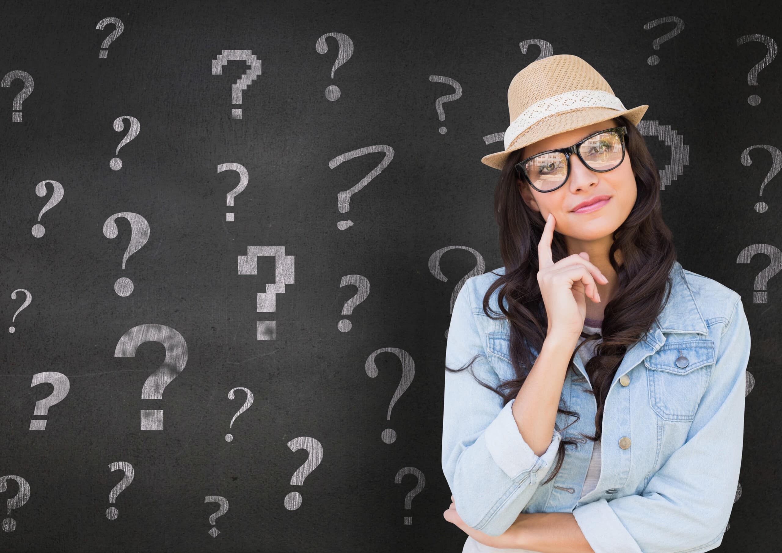 Portrait of a thoughtful woman in straw hat standing in front of chalkboard with question marks
